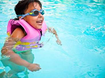child swimming while wearing life jacket and goggles