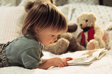 toddler laying on bed looking at book