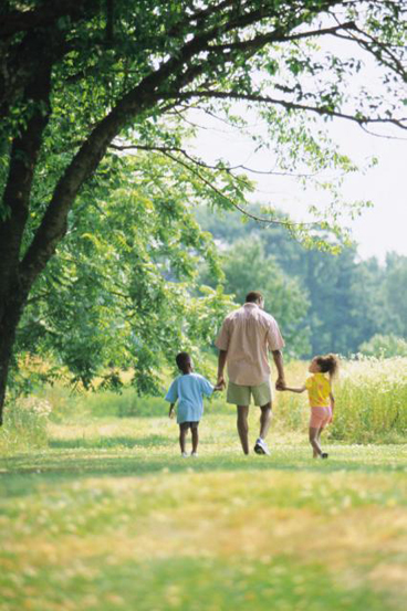 two preschoolers walking with dad in meadow